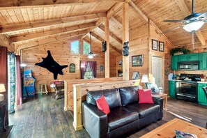 A wooden cabin interior with a black leather sofa, a dining table, and a kitchen area. - A Top Notch Lodge (Gatlinburg)