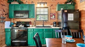 A kitchen with green cabinets, a stainless steel refrigerator, and a dining table with chairs. - A Top Notch Lodge (Gatlinburg)