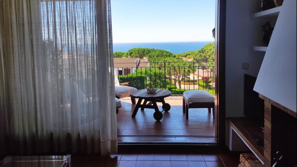 Een balkon met een tafel en stoelen, uitzicht op zee en een bebost gebied.