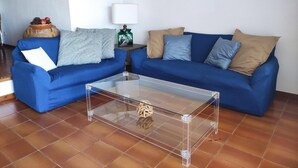 Een woonkamer met twee blauwe banken, een glazen salontafel, een lamp en een gekaderd schilderij aan de muur.