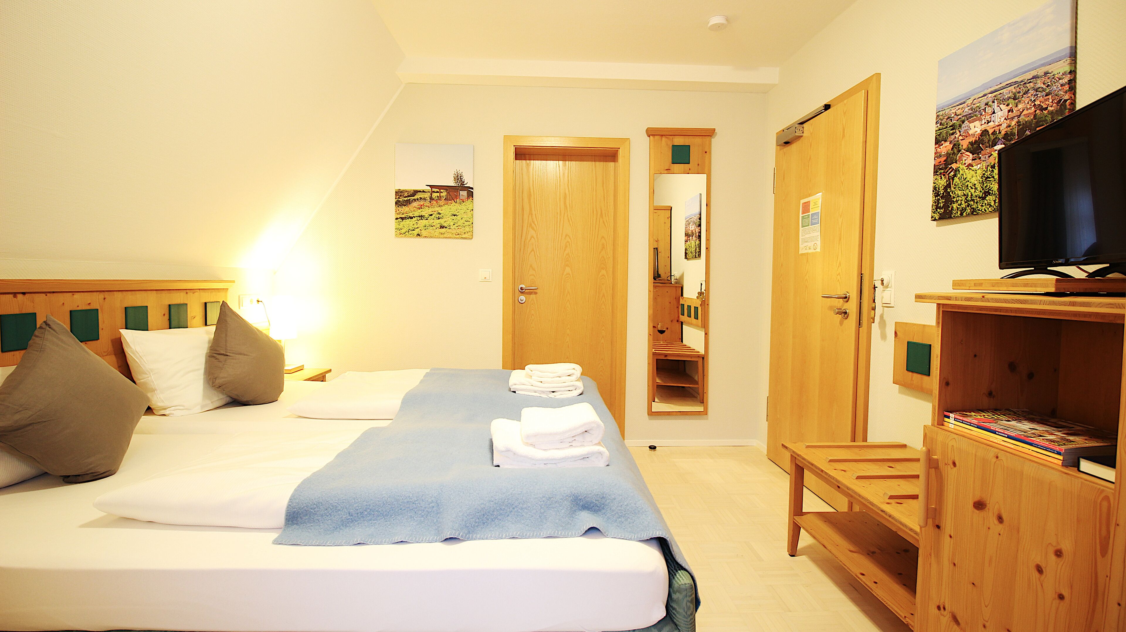 A hotel room with a bed, a TV, a wooden cabinet, and a door leading to a bathroom.