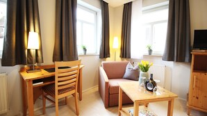 A cozy living room with a wooden desk, a chair, a sofa, and a small table with a bottle and glasses. - Aparthotel Alte Schmiede Dettelbach  (Dettelbach)