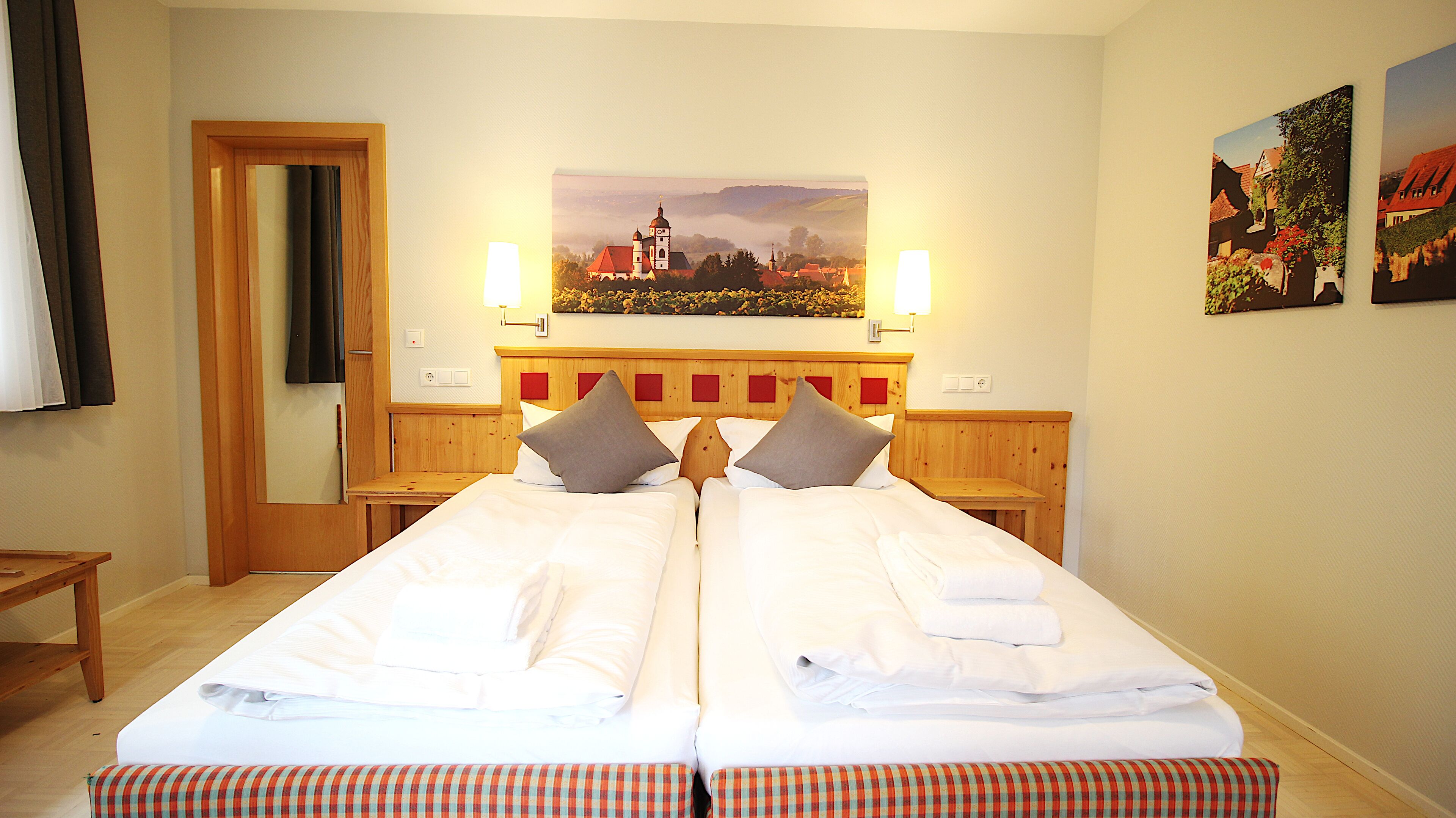 A double bed with a wooden headboard, two bedside tables, and a painting of a village scene above the bed.