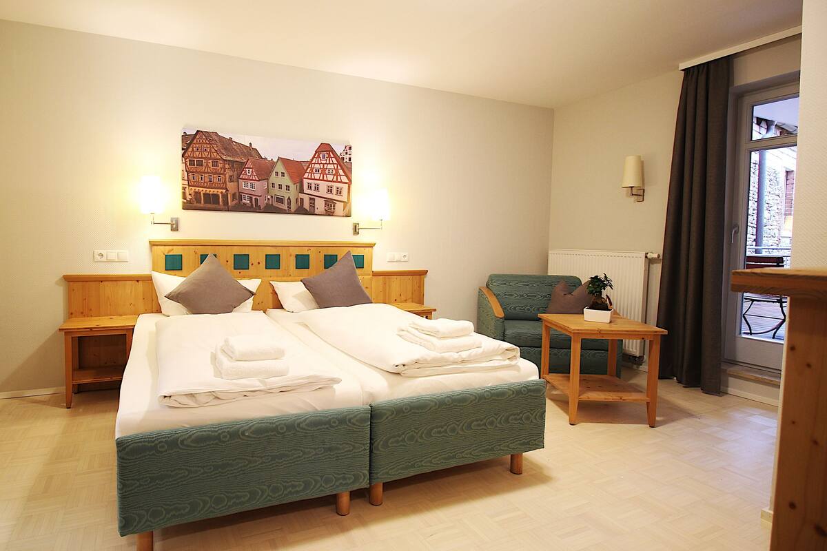 A hotel room with a bed, a chair, a table, a painting, and a window.