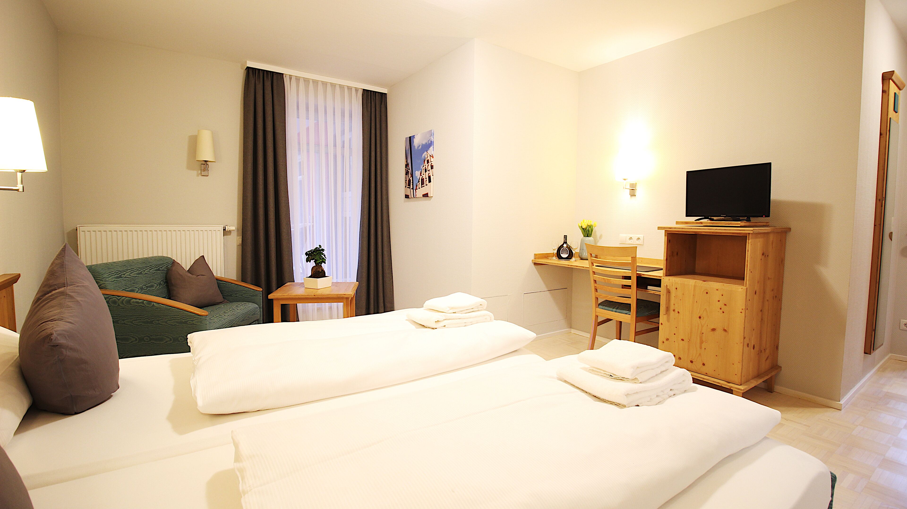 A hotel room with two beds, a desk with a chair, a TV, and a small table with a plant.