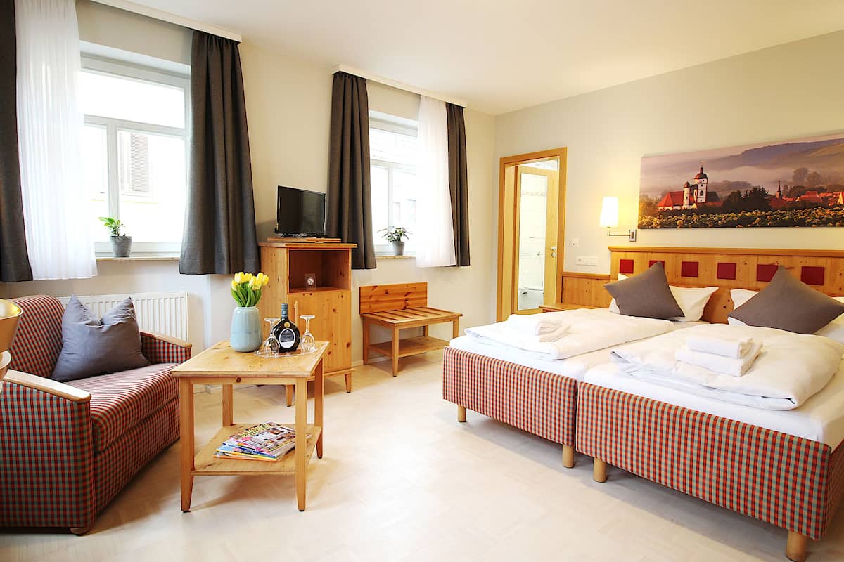 A hotel room with a bed, a sofa, a table with a vase of flowers, a TV, and a painting on the wall.