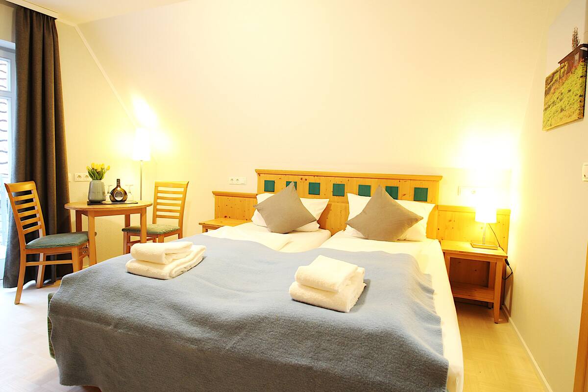 A hotel room with a bed, two bedside tables, a chair, a desk, and a window with curtains.