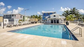 A swimming pool with lounge chairs and a building with a blue and white facade in the background. - Corner of Paradise in Key Largo (Key Largo)