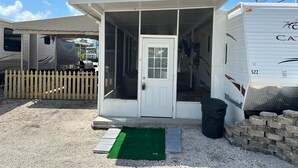 A mobile home with a covered porch, a white door, and a small front yard with a green mat and steps. - Corner of Paradise in Key Largo (Key Largo)