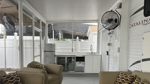 A covered outdoor living area with two beige sofas, a refrigerator, a sink, and a fan. - Corner of Paradise in Key Largo (Key Largo)