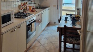 A modern kitchen with white cabinets, a gas stove, and a dining area with a table and chairs. - SUMMER PROMOTION Summer apartment (Viareggio)