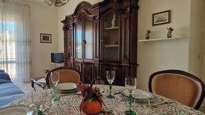 A dining area with a table set for four, surrounded by chairs, a sofa, and a cabinet with glass doors. - SUMMER PROMOTION Summer apartment (Viareggio)