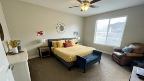 A bedroom with a bed, a desk, a chair, a ceiling fan, and a window.