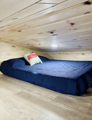 Una habitación pequeña con cama individual, techo de madera y una lámpara.
