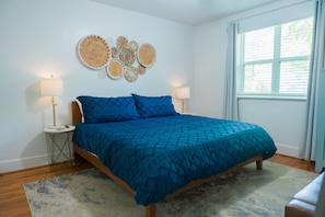 A bedroom with a bed, two bedside tables, wall art, and a window with curtains.