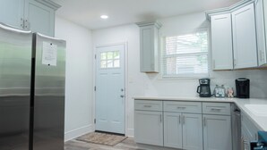 A kitchen with white cabinets, a stainless steel refrigerator, a coffee maker, and a window with blinds. - Modern 2BR King Bed near USC, Downtown & Ft Jackson (Columbia)