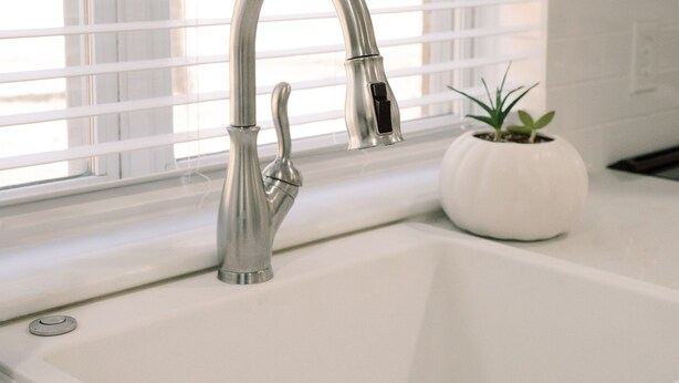 A white kitchen sink with a modern faucet, a potted plant, and a window with blinds. - Modern 2BR King Bed near USC, Downtown & Ft Jackson (Columbia)