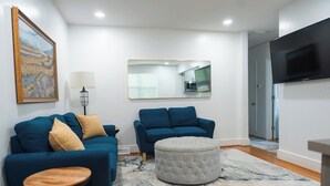 A living room with two sofas, a round ottoman, a lamp, a painting, and a TV. - Modern 2BR King Bed near USC, Downtown & Ft Jackson (Columbia)