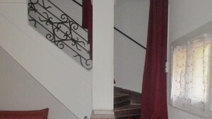 Una escalera con una cortina roja, una silla y un cojín rojo en una habitación con paredes blancas.