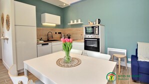 Una cocina moderna con armarios blancos, horno empotrado y comedor con mesa y sillas.
