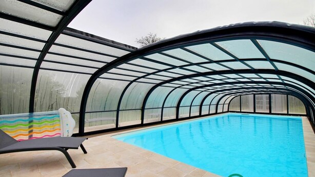 Una piscina interior con techo de cristal, sillas de descanso y suelo de baldosas.