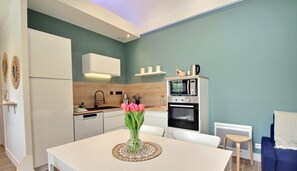 Una cocina moderna con armarios blancos, horno empotrado y comedor con mesa y sillas.