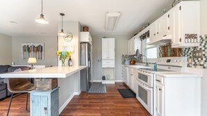 A modern kitchen with white cabinets, a central island, and a dining area with a sofa. - Life on the Lake. Enjoy the peace and kayaks. (Locust Grove)