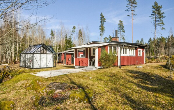 Punainen puutalo, jossa on lasinen kasvihuone, ja sen ympärillä on metsää.
