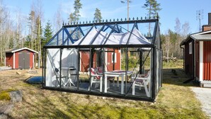 Een glazen broeikasconstructie met metalen frame, een tafel en stoelen van binnen.