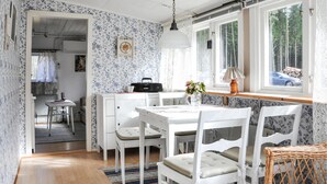 Een gezellige keuken met witte kasten, een eettafel en stoelen. Er is een raam met uitzicht op bomen en een auto buiten.