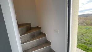 Eine Treppe mit grauen Fliesen führt zu einem Balkon mit Blick auf ein grünes Feld und ferne Hügel.