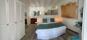 A bedroom with a bed, bedside tables, a dresser, a walk-in closet, and a large abstract painting.