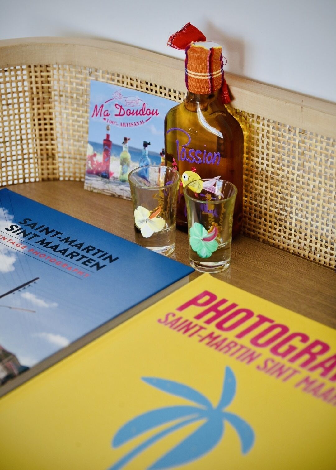 A bottle of Passion wine, two glasses with flowers, and books titled 'Saint-Martin' and 'Photogra Saint-Martin'.