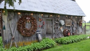 Ein rustikales Getreidespeichergebäude mit Holzfassade, verziert mit verschiedenen Dekorationen, darunter ein großer Kranz, ein Schild mit der Aufschrift „HORSE TACK“ und weitere Gegenstände.