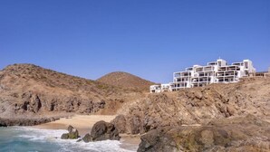 A coastal hotel with a rocky shoreline, waves crashing against the rocks, and a clear blue sky. - Oceanfront at Cerritos Beach • Infinity Pool+Spa (Los Cerritos)