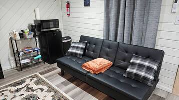 Un salon moderne avec un canapé en cuir noir, deux coussins, une petite table basse, un four à micro-ondes, un extincteur et une étagère contenant divers objets.