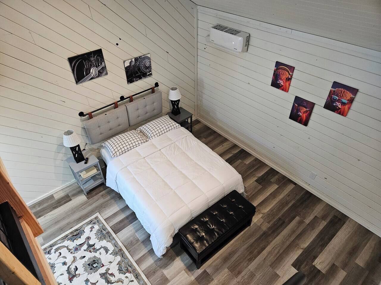 Une chambre à coucher comprenant un lit, des tables de chevet, un tapis et des œuvres d’art accrochées au mur.