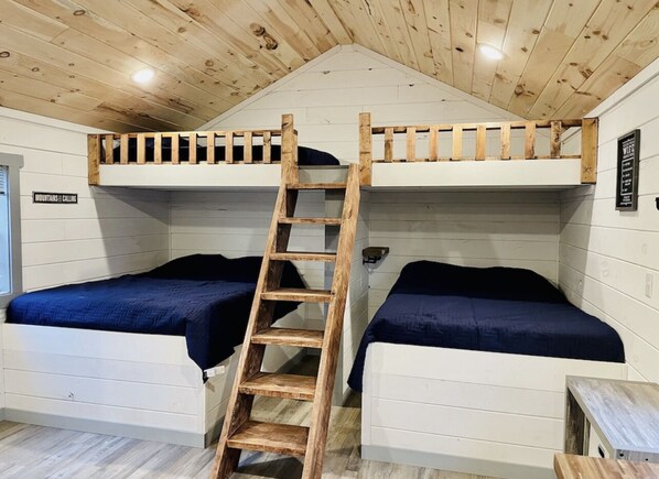 A bunk bed room with a wooden ladder, white walls, and a small table.