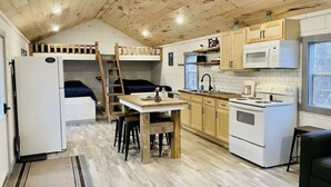 A compact kitchen with wooden ceiling beams, a built-in bench, a refrigerator, a stove, and a microwave. - UTV/ATV PARADISE! A/C and heat  (Huntsville)