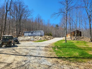 A gravel path leading to a cabin with a metal shed and a wooden structure in a forested area.