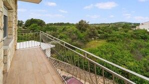 A balcony with a stone wall, a metal railing, and a view of a green landscape with trees and hills. - Beautiful apartment in Gornje Selo with WiFi (Gornje Selo)