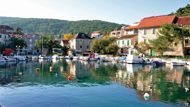 A marina with boats docked, surrounded by stone buildings with red roofs and green shutters, set against a backdrop of green hills. - Beautiful apartment in Gornje Selo with WiFi (Gornje Selo)