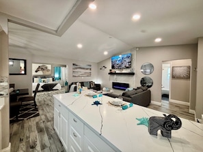 A modern living room with a large TV, a fireplace, and a dining area with a marble island.