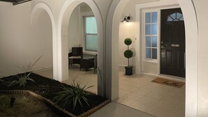 Un hall d’entrée bien éclairé avec une porte sombre, un petit coin salon avec une table et des chaises, et une plante en pot.