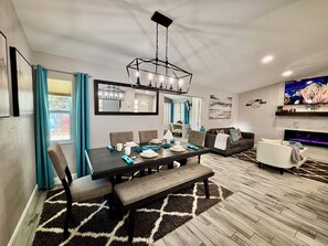 A modern living room with a dining area, a sofa, a TV, and a fireplace.