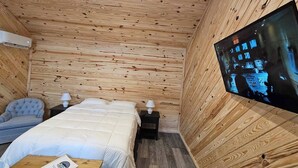 Une pièce aux murs lambrissés, contenant un lit, une chaise, une table et un téléviseur.