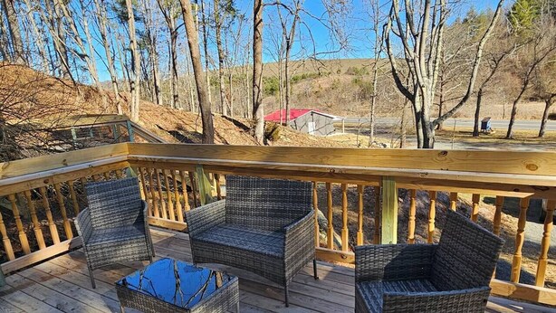 Une terrasse en bois, agrémentée de meubles en osier et d’une petite table, entourée d’arbres et d’un bâtiment situé au loin.