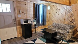 Une pièce de taille modeste, avec un intérieur en bois, un canapé, une petite table, un four à micro-ondes et une porte dotée d’une fenêtre.