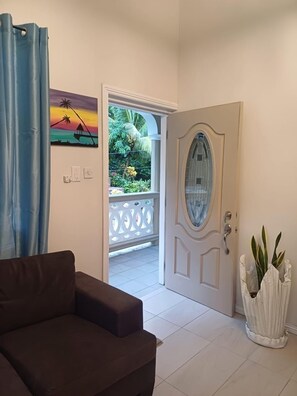 Una habitación con un sofá marrón, una puerta blanca con paneles de vidrio, un cuadro de un atardecer y una planta en maceta.