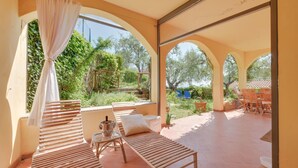A sunlit patio with wooden loungers, a small table with a bottle and glasses, and a view of greenery and trees. - Beautiful home in Diano Calderina (Diano Calderina)